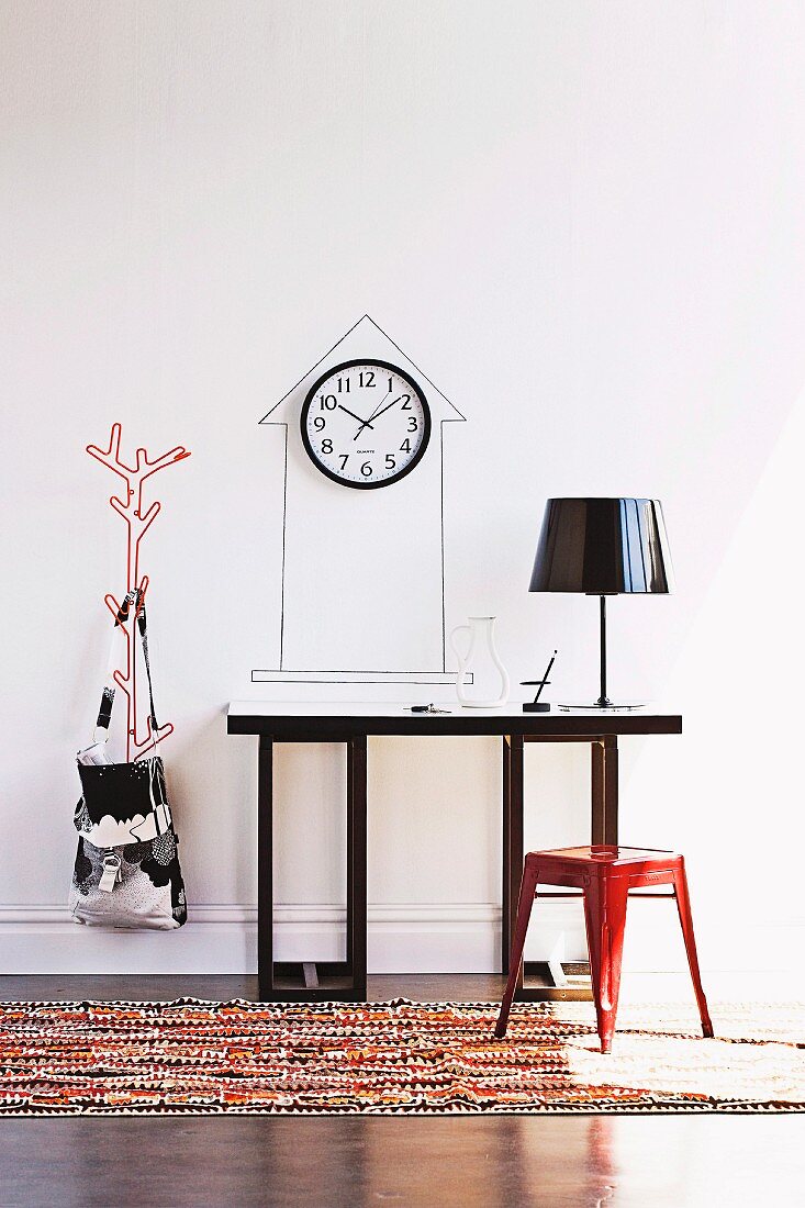 Red, retro metal stool at console table with table lamp; clock on wall in outline of tower