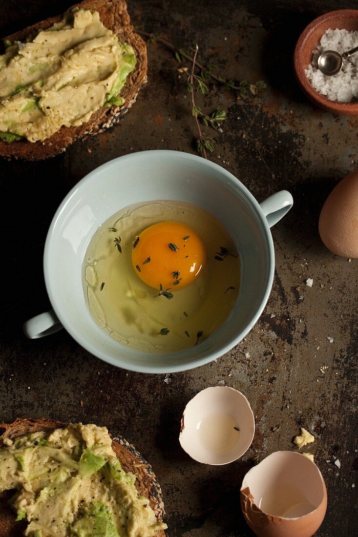 Aufgeschlagenes Ei und Brote mit Avocadoaufstrich