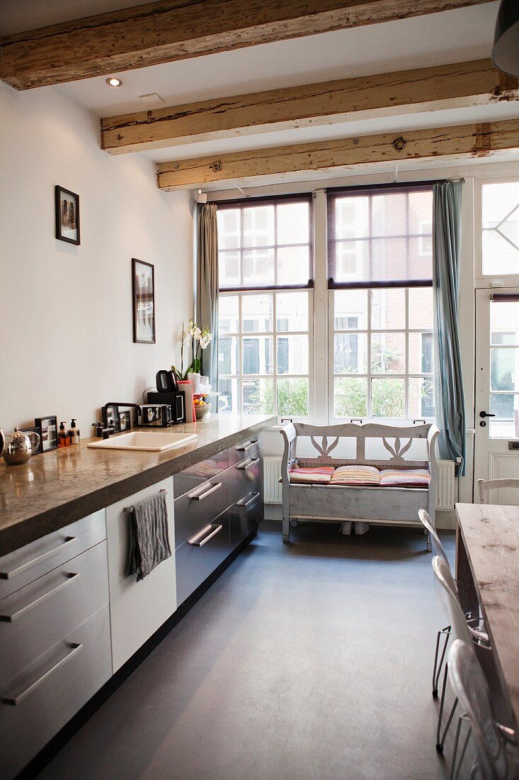 Kitchen counter with stainless steel fronts and rustic bench below lattice window