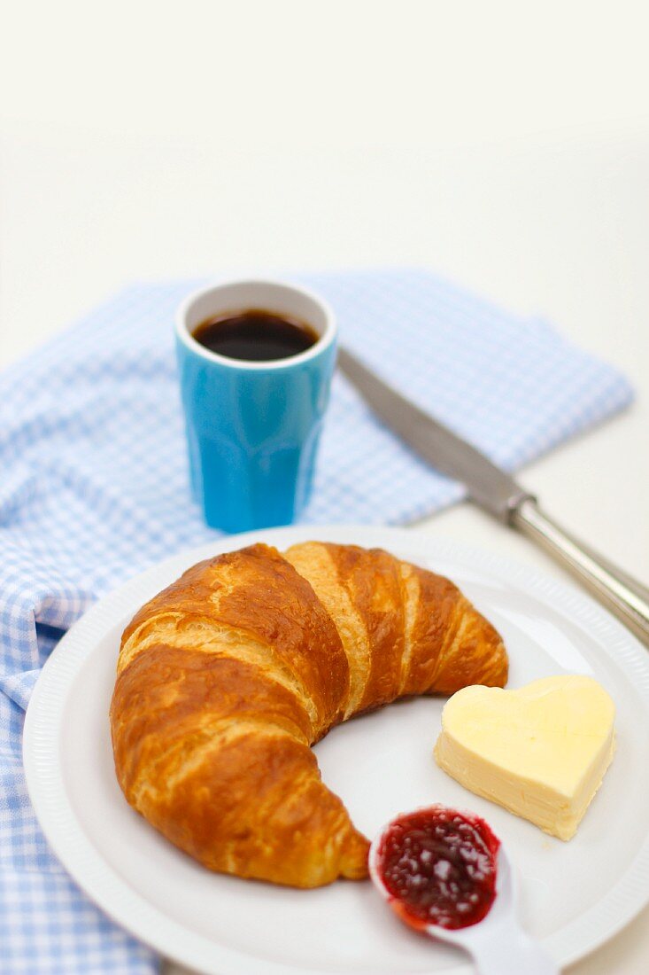 Croissant with jam and a heart-shaped pat of butter, and a cup of coffee