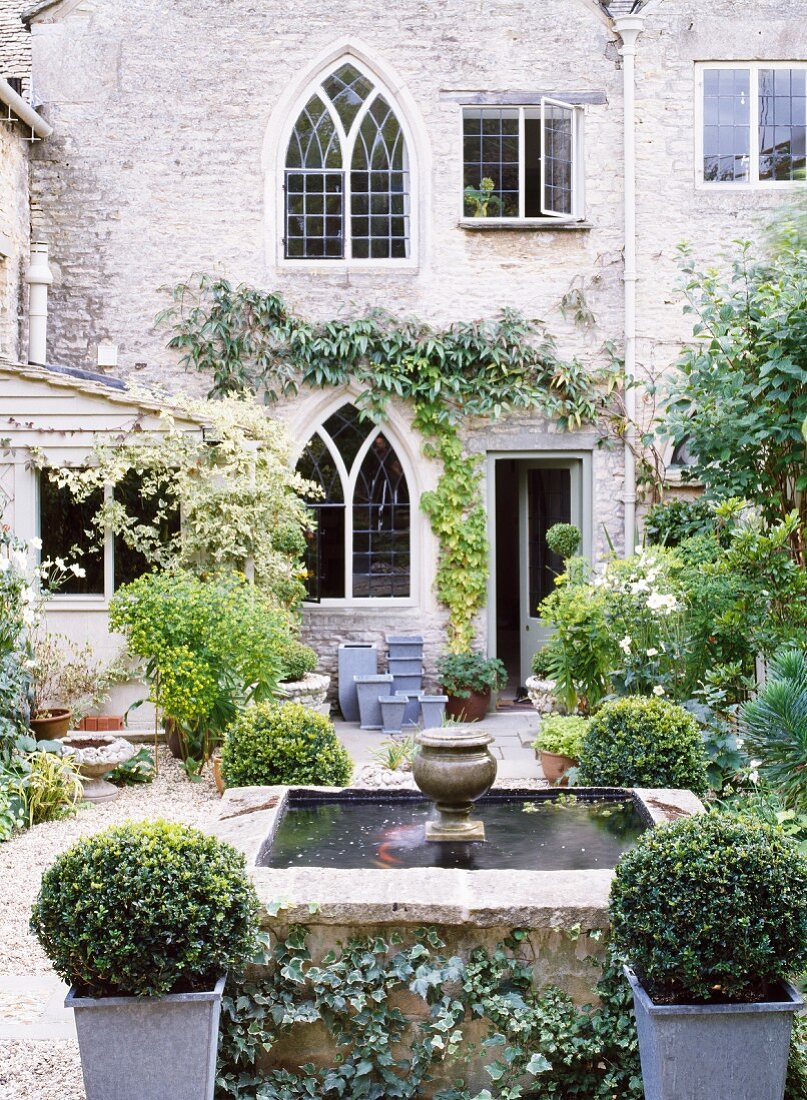 Begrünter Innenhof eines Landhauses im gotischen Stil mit Buchsbäumen um Brunnen