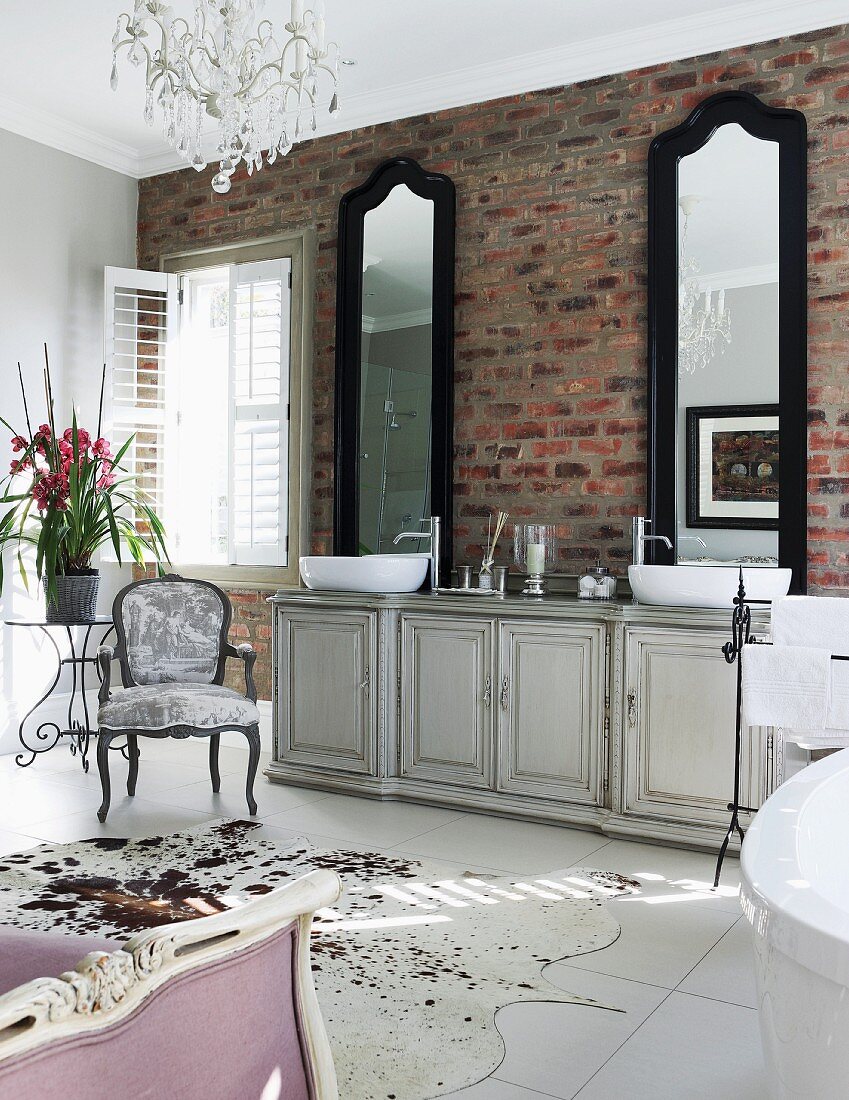 Two tall mirrors above vintage washstand cabinet against brick wall in shabby chic bathroom
