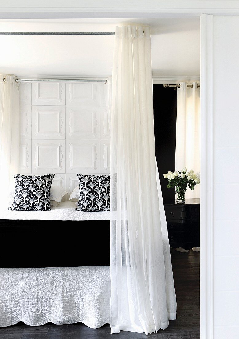 Elegant double bed with black and white textiles and floor-to-ceiling curtains hanging from encircling rod