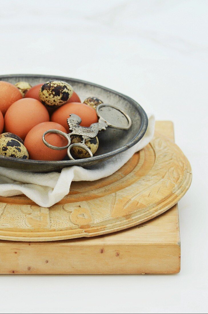 A metal bowl of quail and chicken eggs on a pile of wooden chopping boards