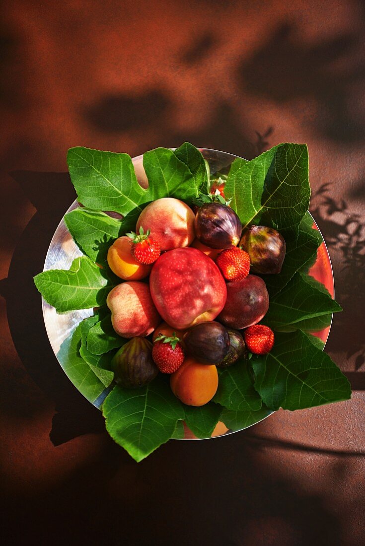 Assorted fresh fruits on fig leaves (view from above)