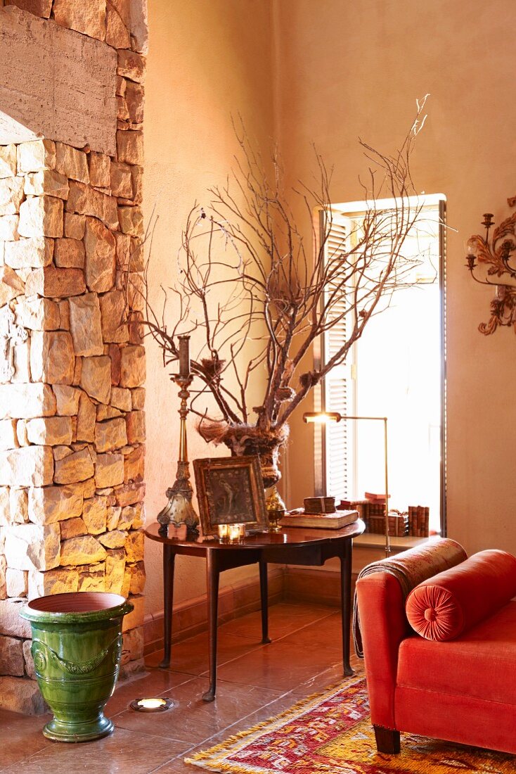 Corner of room in grand country house with round table and floor vase next to stone column and red chaise longue