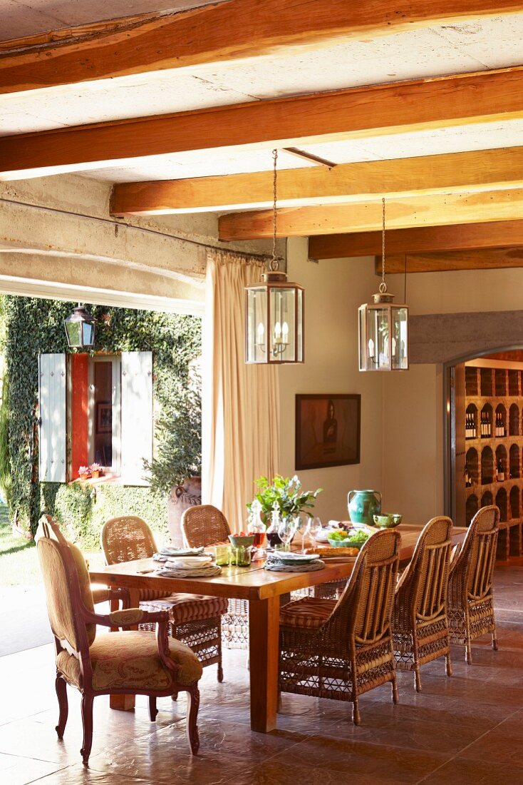 Rattan chairs in dining area in rustic interior with open terrace door and view of garden