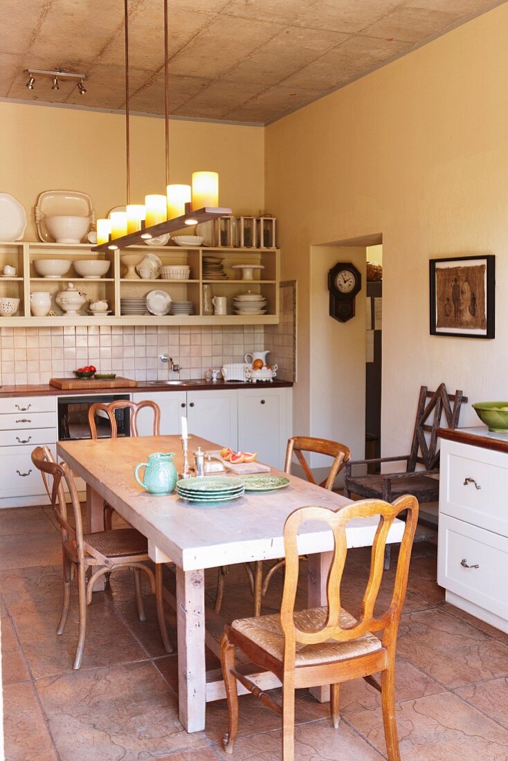 Rustic dining table and chairs with curved backrests below candle lanterns suspended from exposed concrete ceiling in simple interior