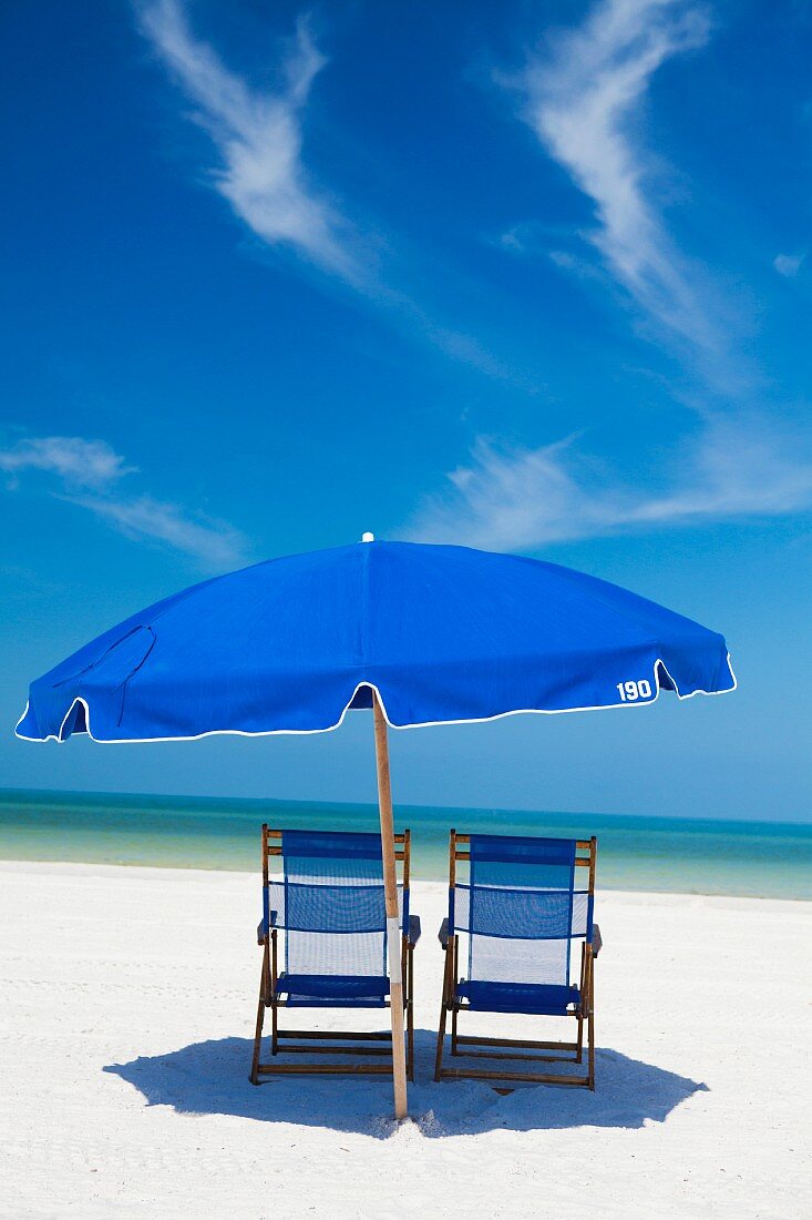 Blauer Sonnenschirm und Liegestühle mit blauem Bezug am Meer