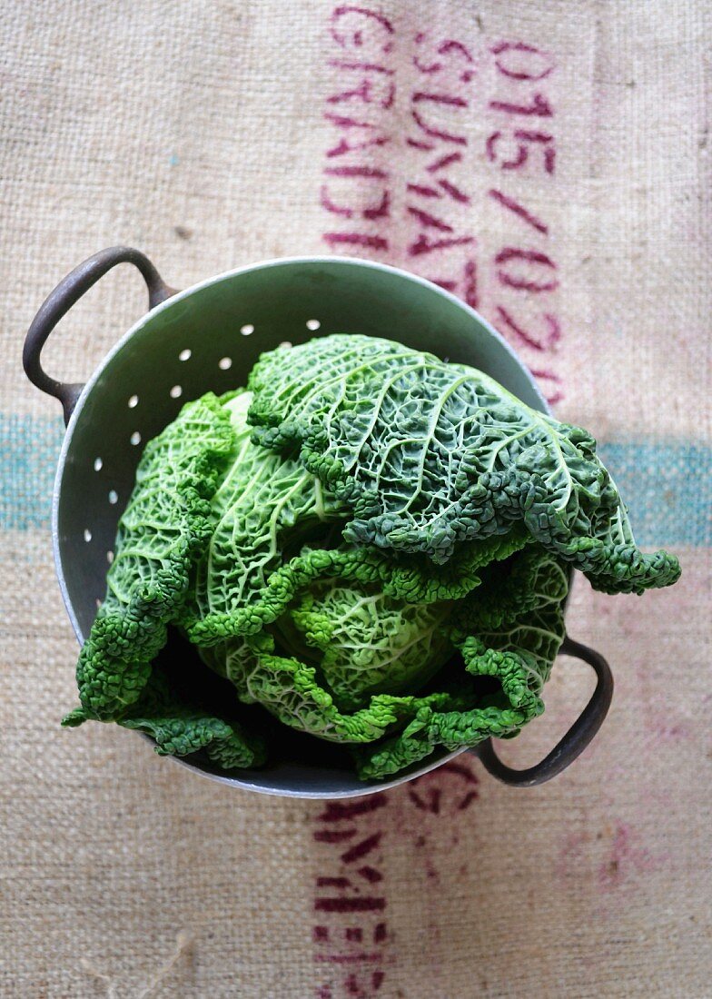 A savoy cabbage in a vintage colander on a printed hessian coffee sack