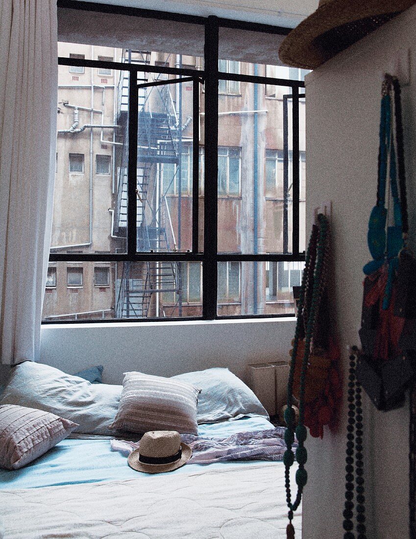 Doppelbett in Schlafzimmer mit Industriefenster und mit Blick auf Feuertreppe und Fensterfronten des Nachbargebäudes