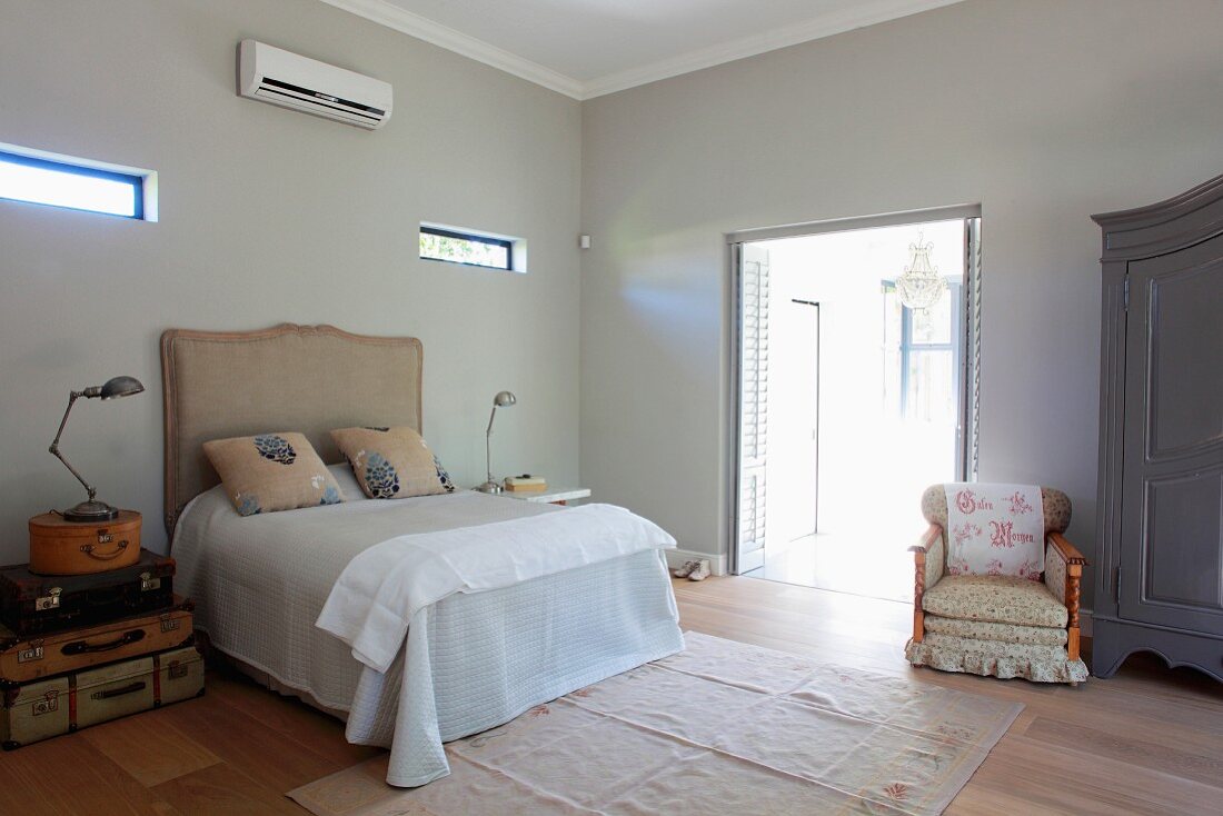 Doppelbett mit gepolstertem Kopfteil und Sessel neben offener Terrassentür in minimalistischem, klimatisiertem Schlafzimmer