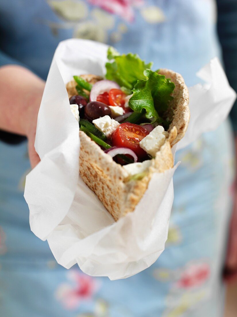 A woman holding a pita bread filled with Greek salad