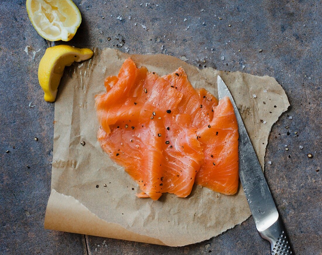 Smoked salmon, a knife and lemon wedges on grease-proof paper
