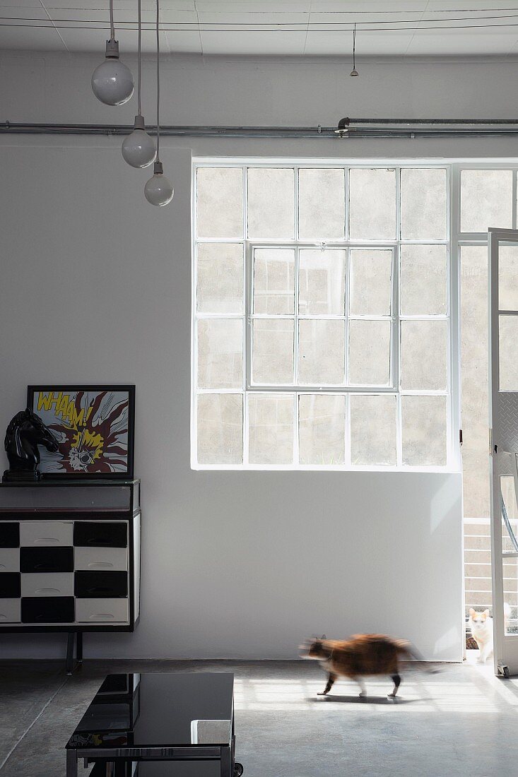 Offene Fenstertür neben rechteckigem Industriefenster; an der Wand ein schwarz-weiss gemustertes Sideboard mit einem Pferdekopf und einer Zeichnung