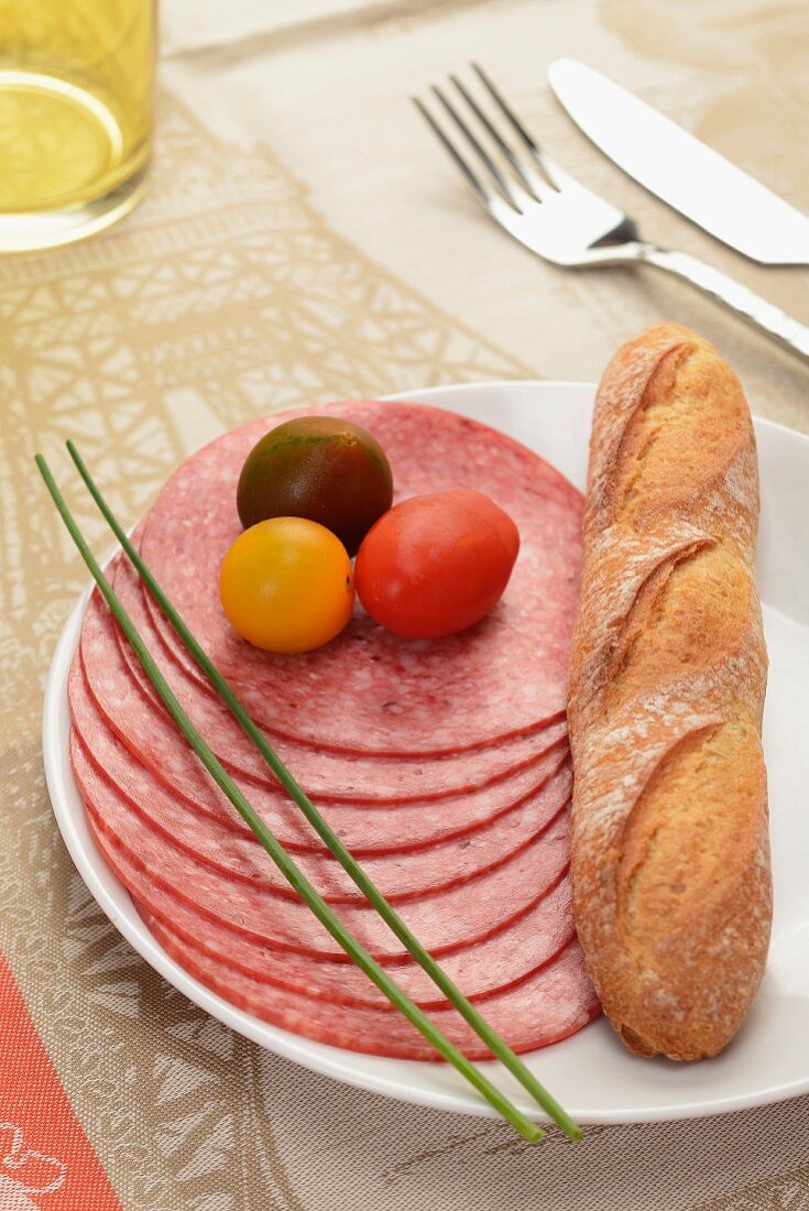 Several slices of smoked salami with cherry tomatoes and a baguette
