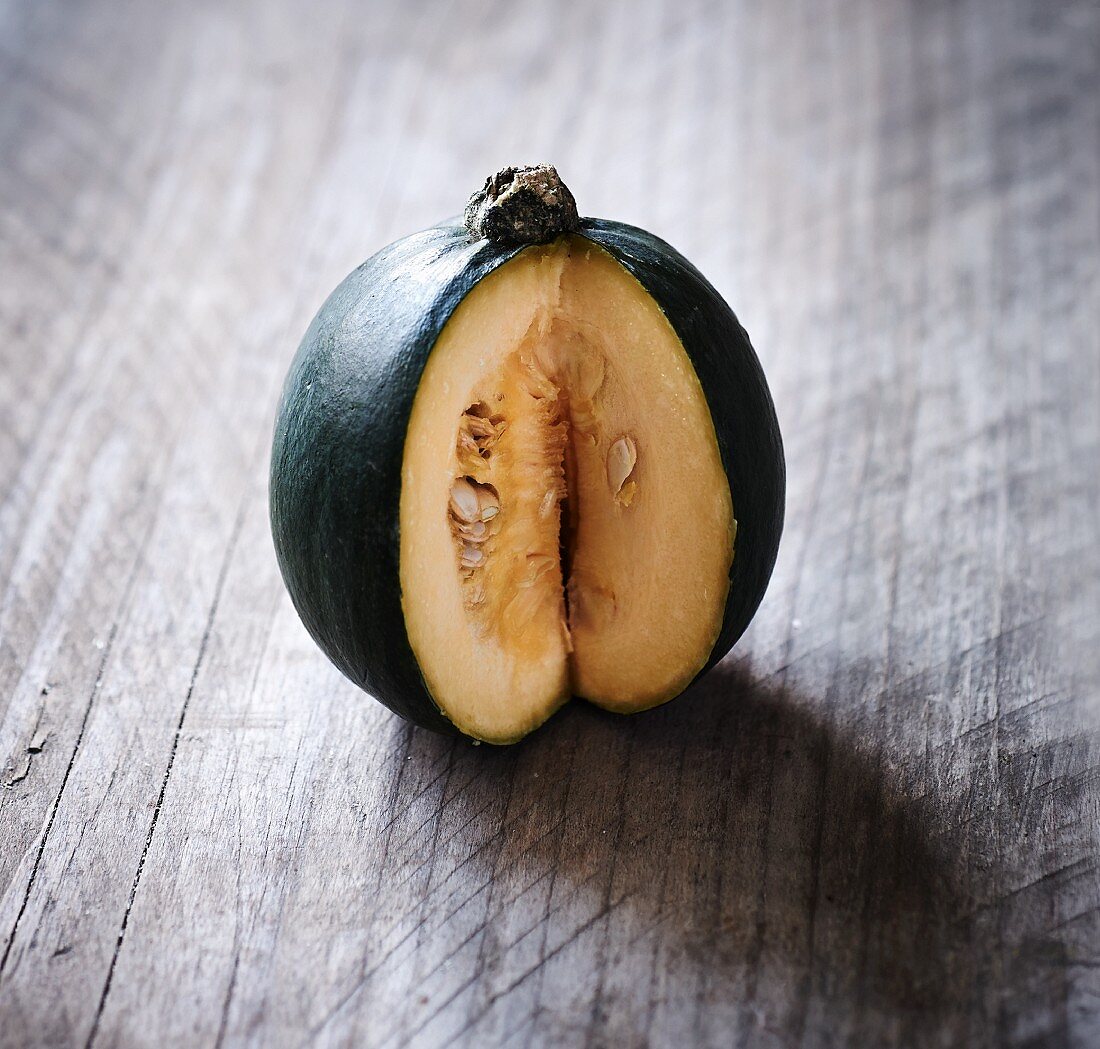 A green squash, sliced to show the centre, on a wooden surface