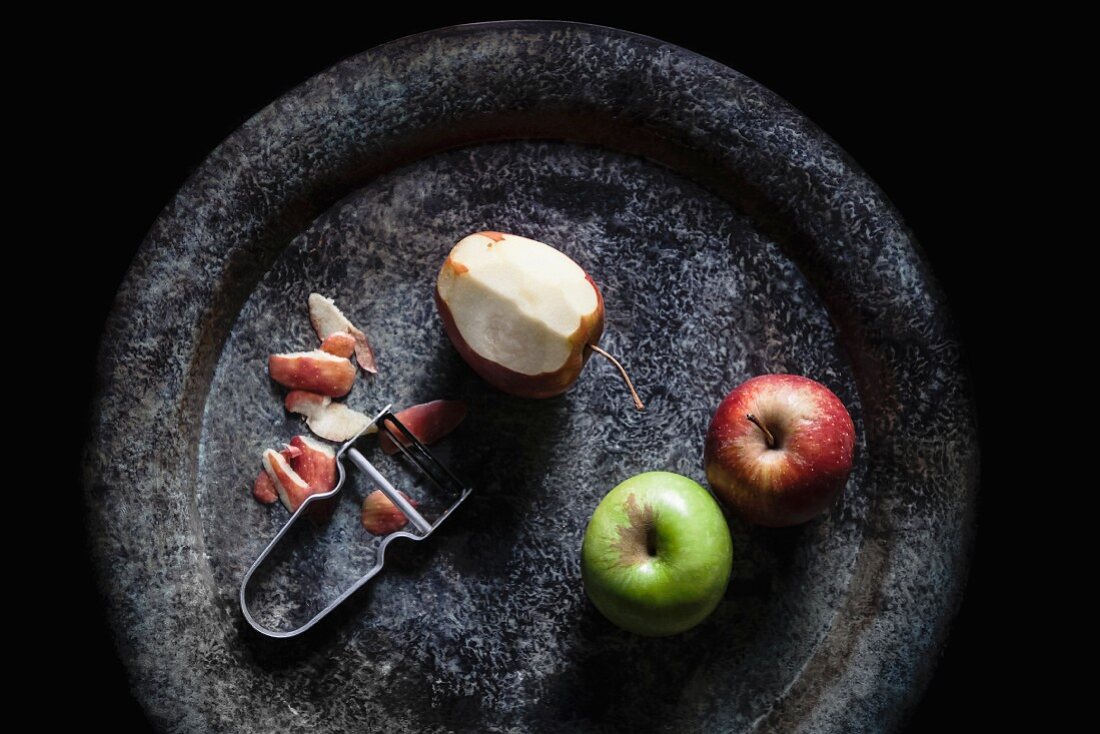 Three apples with a peeler on a stone plate