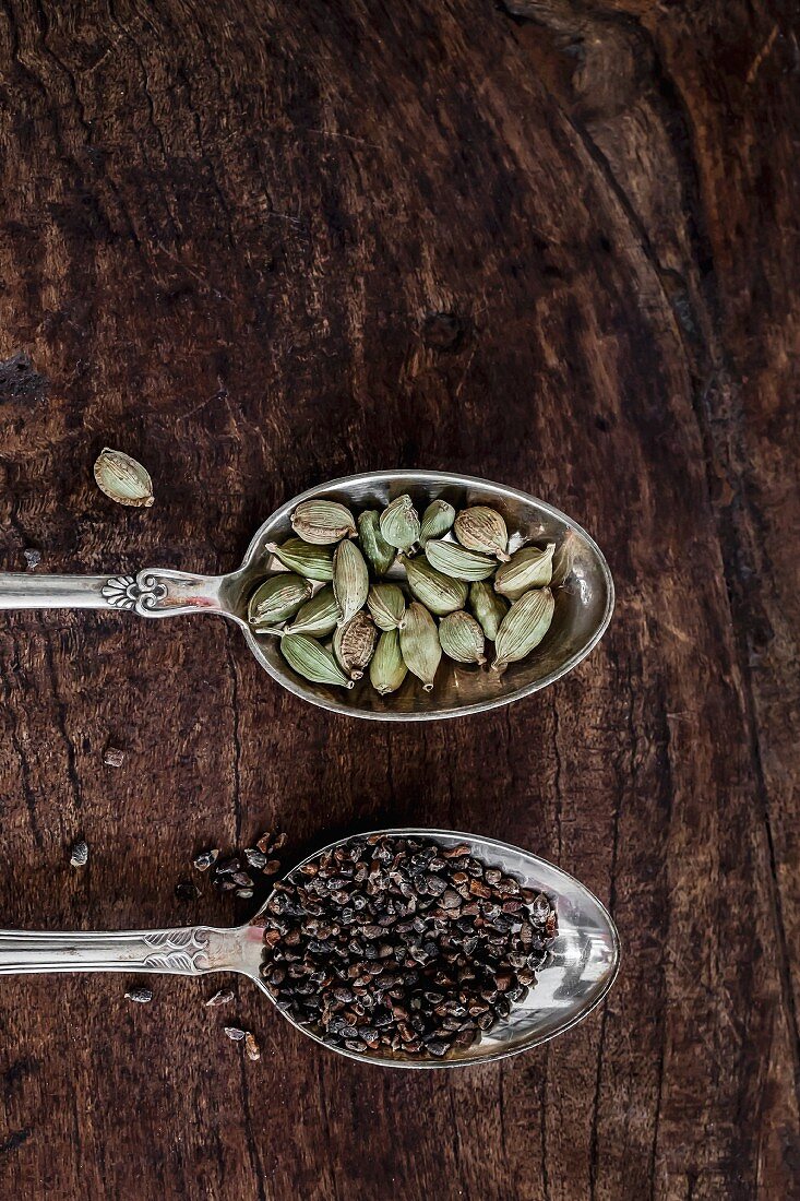 Cardamom on silver spoons on a wooden surface