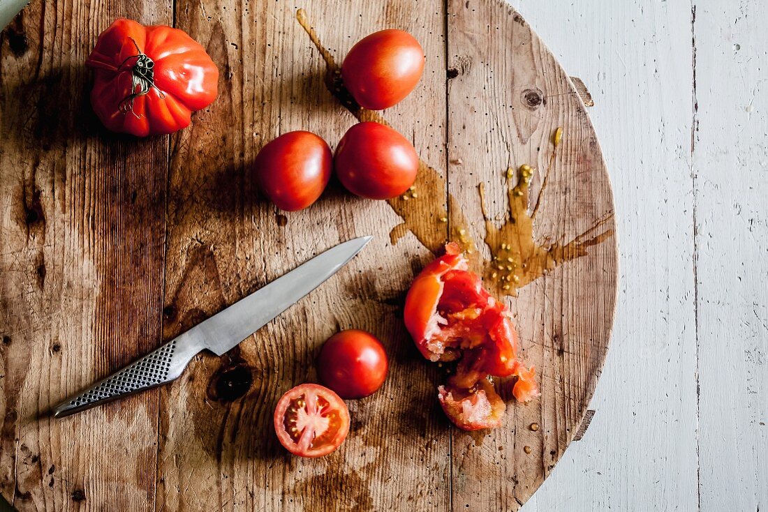 Mehrere Tomaten, teilweise geschnitten und zerdrückt, auf rundem Holzbrett