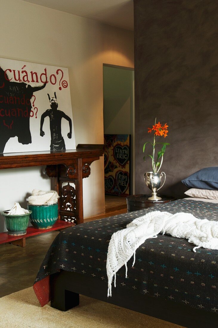 Bedroom with brown partition and modern painting on antique console table; red flowers in silver vase on bedside table