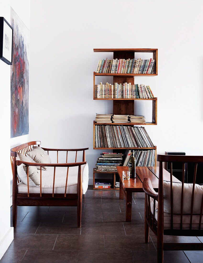 Unusual, winding bookshelves against white wall in simple, bright living room with delicate wooden furniture
