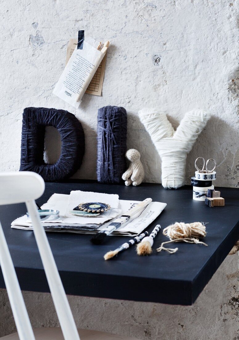 Mit blauer und weisser Wolle umwickelte Pappbuchstaben auf Schreibtischplatte vor grob verputzter Wand aufgestellt