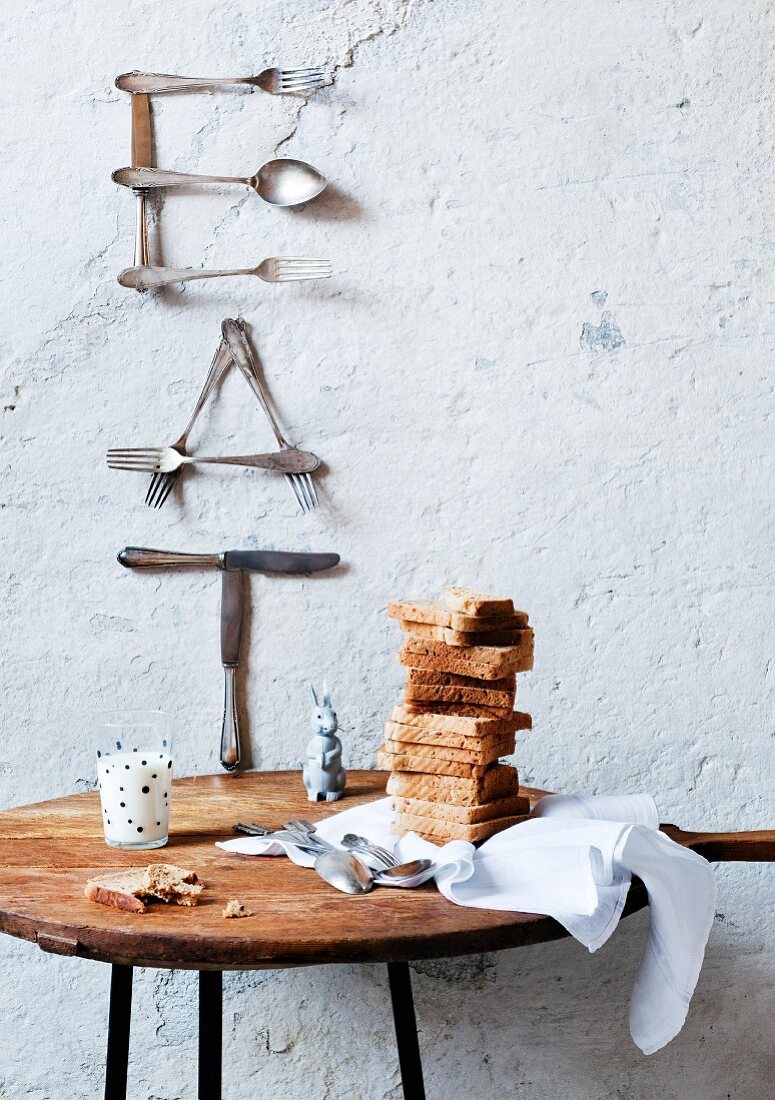 Hand-crafted wall decoration of letters made from old cutlery; cloth, stacked toast and glass of milk on round table