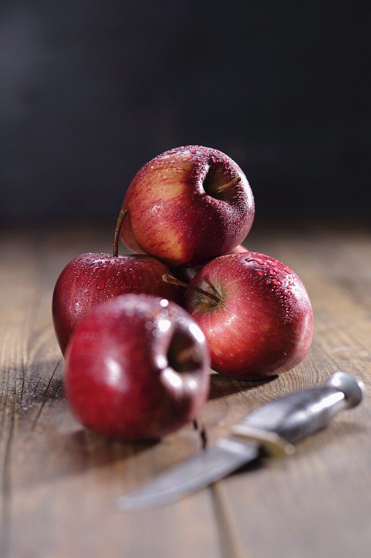 Rote Äpfel mit Wassertropfen und Messer auf Holzuntergrund