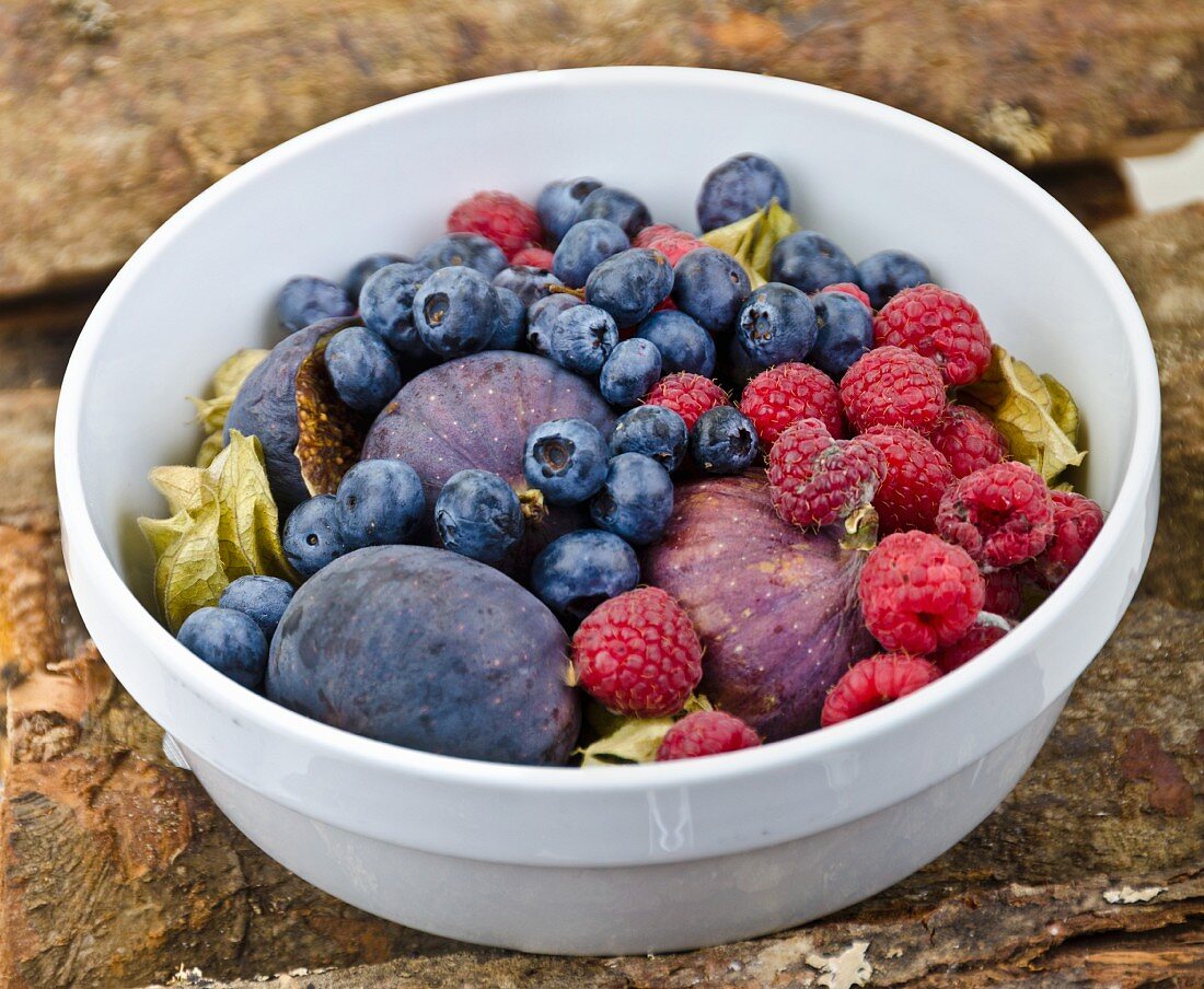 A fruit bowl with figs, blueberries and raspberries on a wooden surface