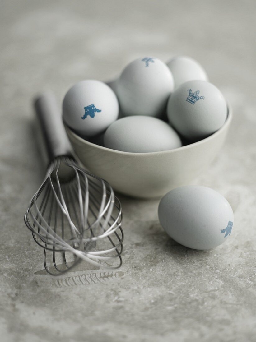 Eggs with a crown stamp in a bowl next to an egg whisk