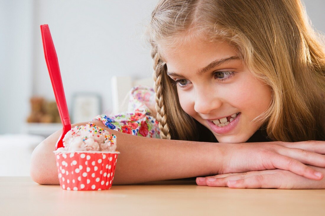 A girl sitting and looking expectantly by a cup of ice cream