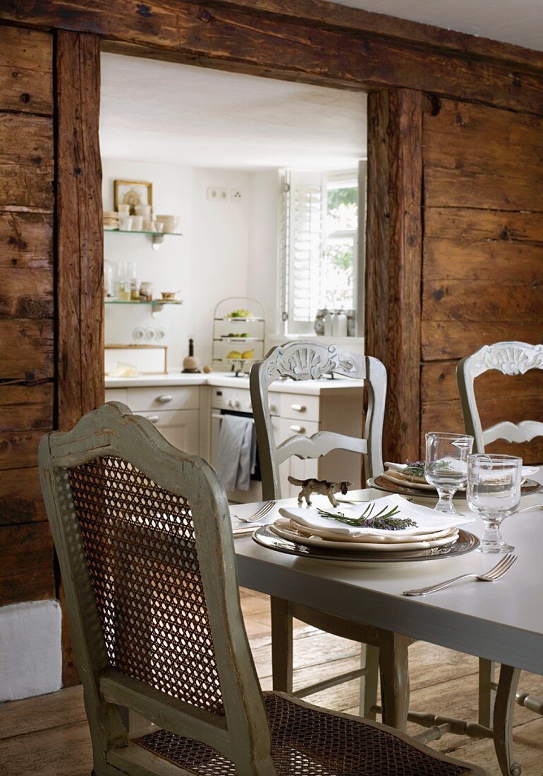 Antike französische Stühle mit grau lackiertem Holzrahmen an handgefertigtem italienischen Esstisch vor Durchgang zur Küche