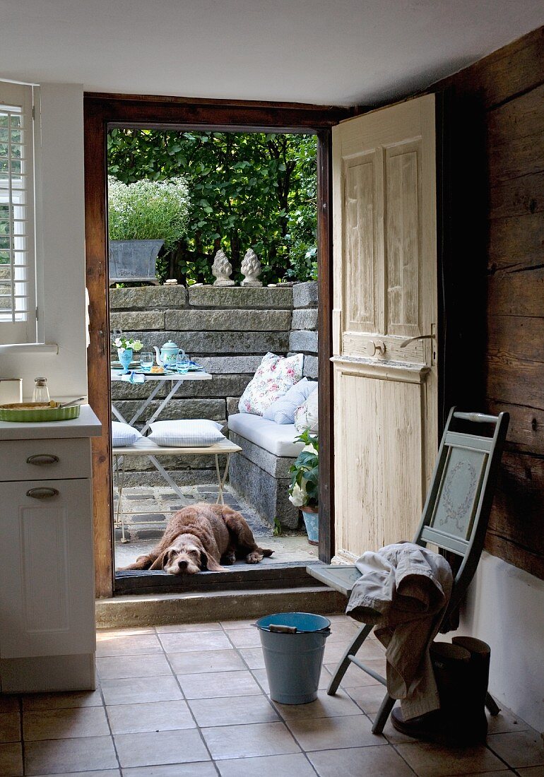 Küche mit offener Holztür und Blick auf Terrasse mit Hund vor Tisch und Bank an Steinmauer