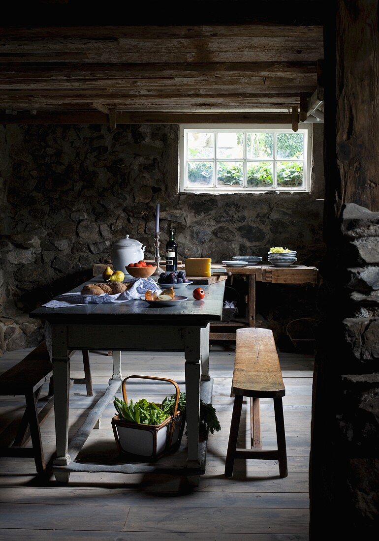 Holztisch mit bayerischer Brotzeit und rustikale Sitzbänke im Kellerraum mit Steinmauern