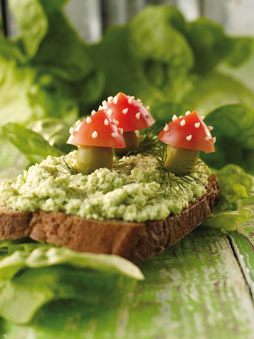 A slice of bread topped with spinach pâté and toadstools made from tomatoes and olives