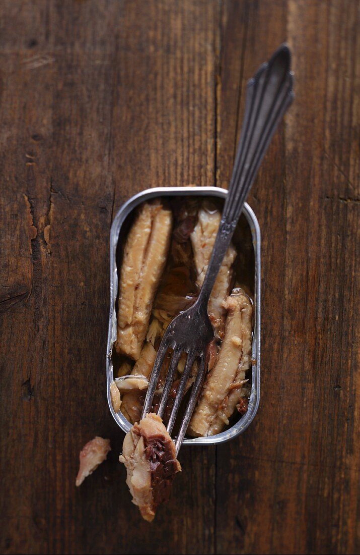 An open can of sardines with a fork on a wooden table