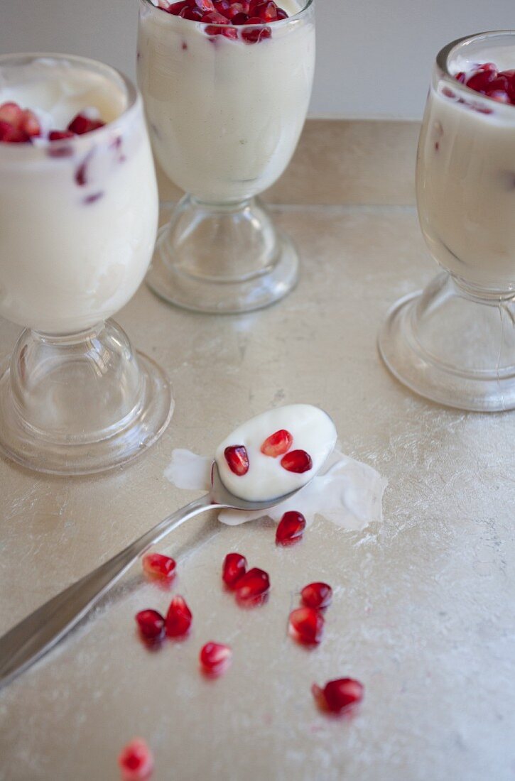Joghurt mit Granatapfelkernen in drei Gläsern und auf Löffel