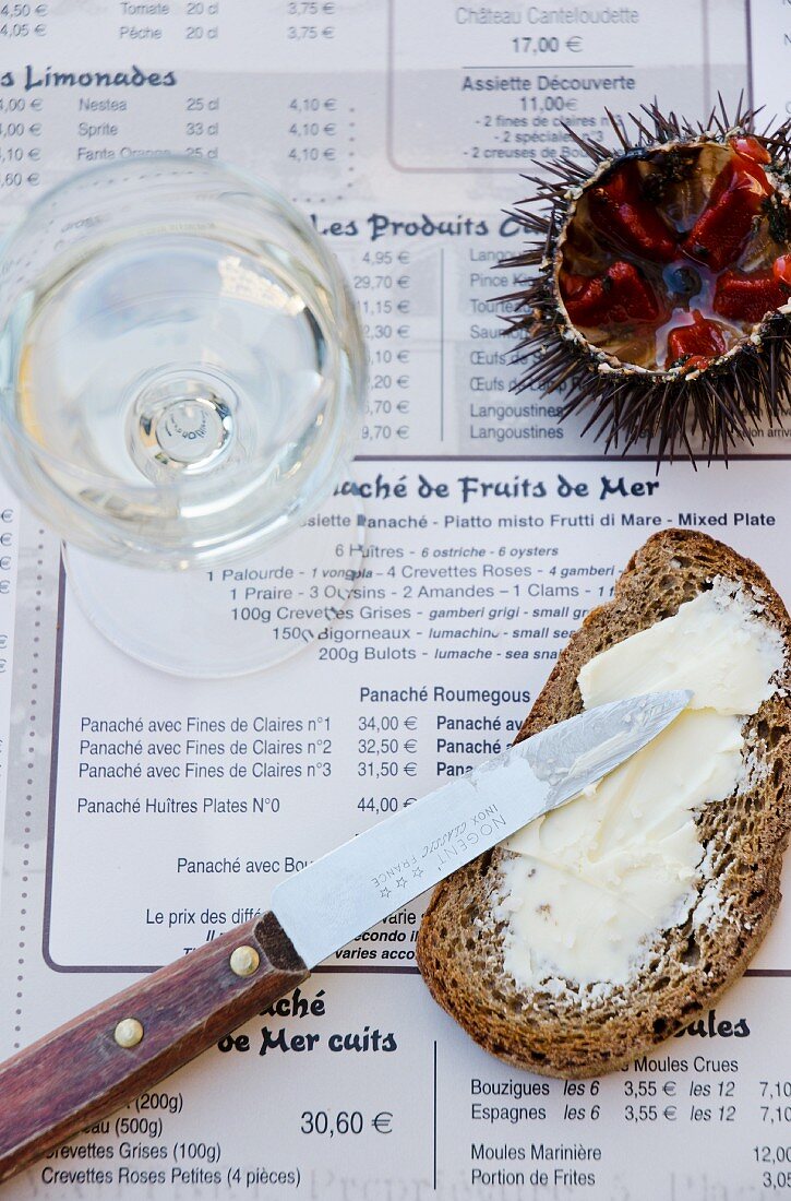 A slice of buttered bread, a sea urchin and a glass of white wine on a menu