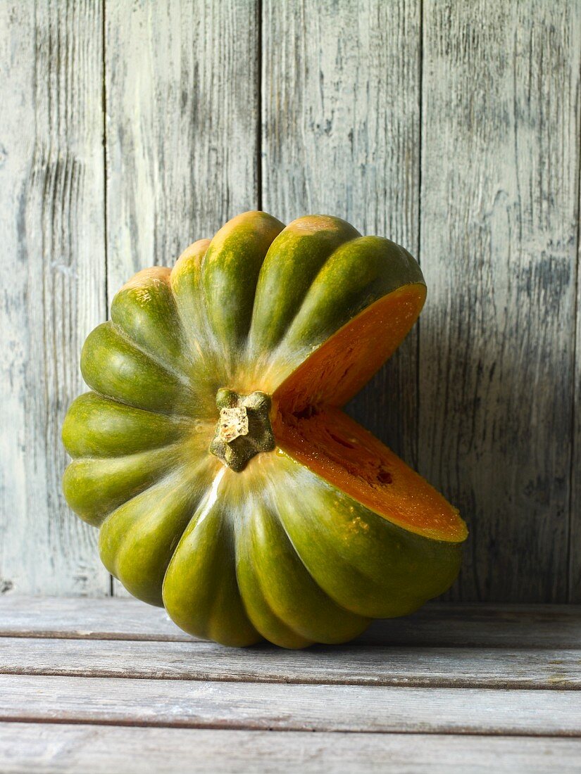 A green winter squash, cut open, against a wooden wall