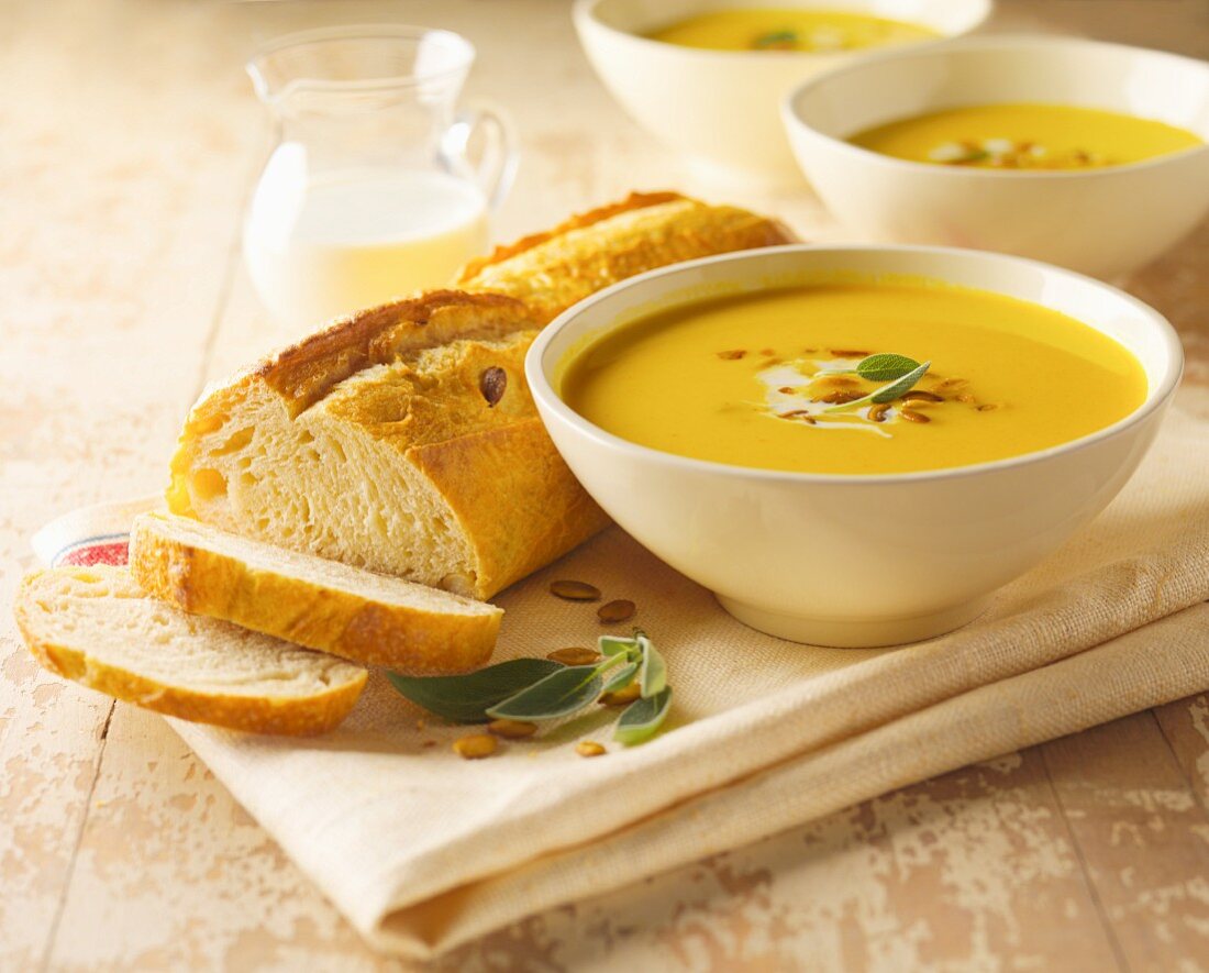 Kürbissuppe mit Salbei und Kürbiskernen, angeschnittenes Brot