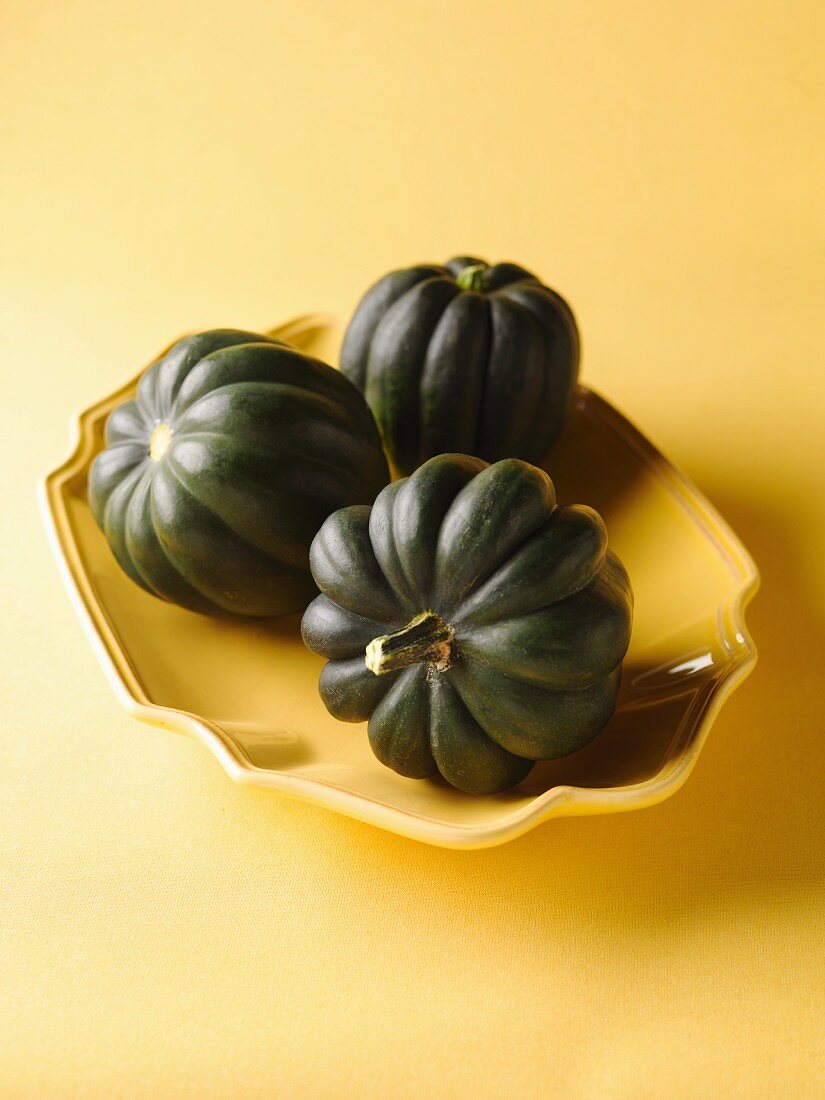 Three Whole Acorn Squash in a Shallow Yellow Bowl; Yellow Background