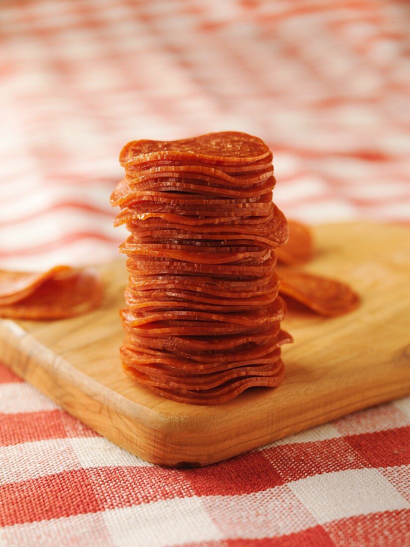 Stacked Pepperoni on a Cutting Board on a Red and White Checkered Cloth