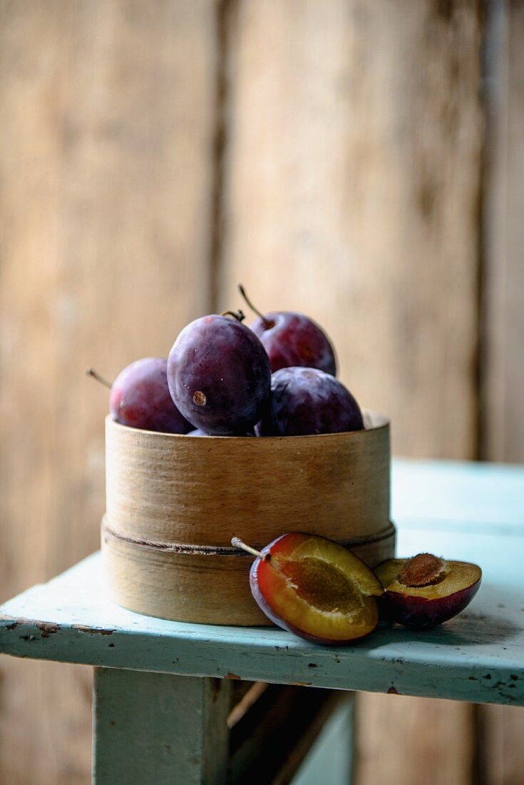 Plums in a woodchip basket on a wooden table