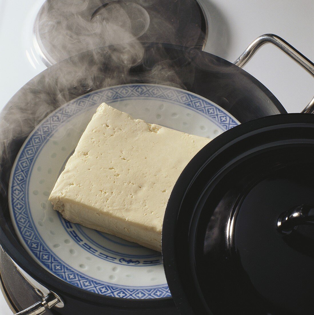Gedämpfter Tofu auf Teller in Kochtopf mit heißem Wasser
