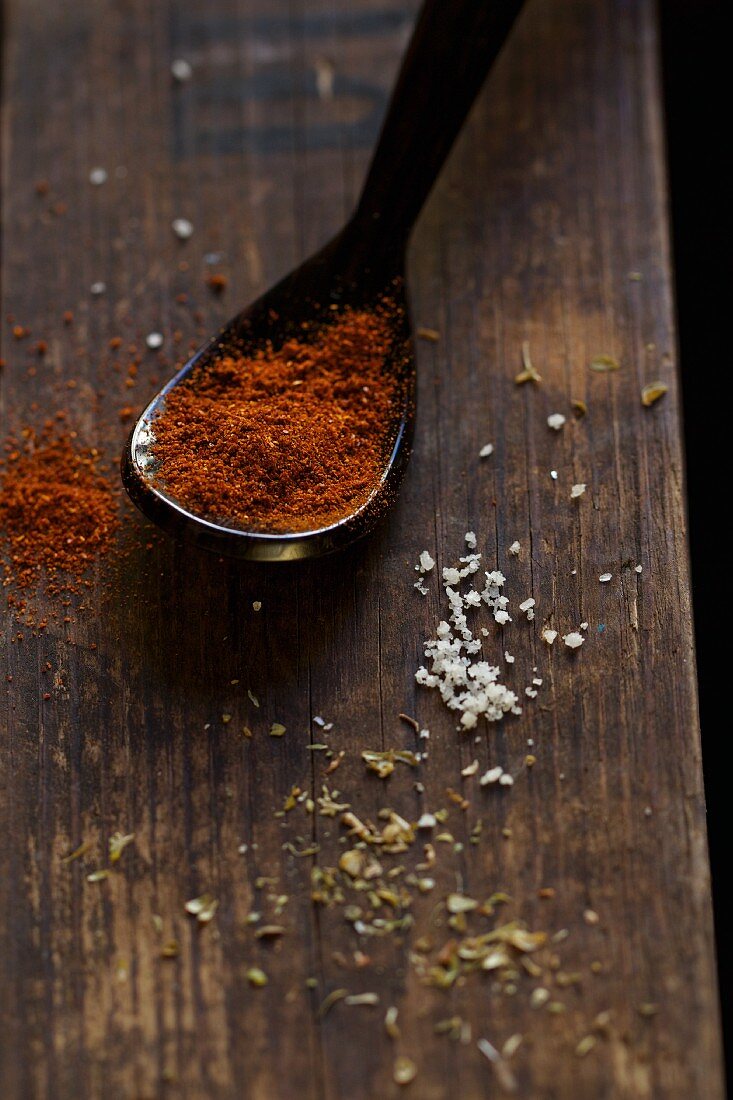A spoonful of chilli powder and assorted spices on a wooden board