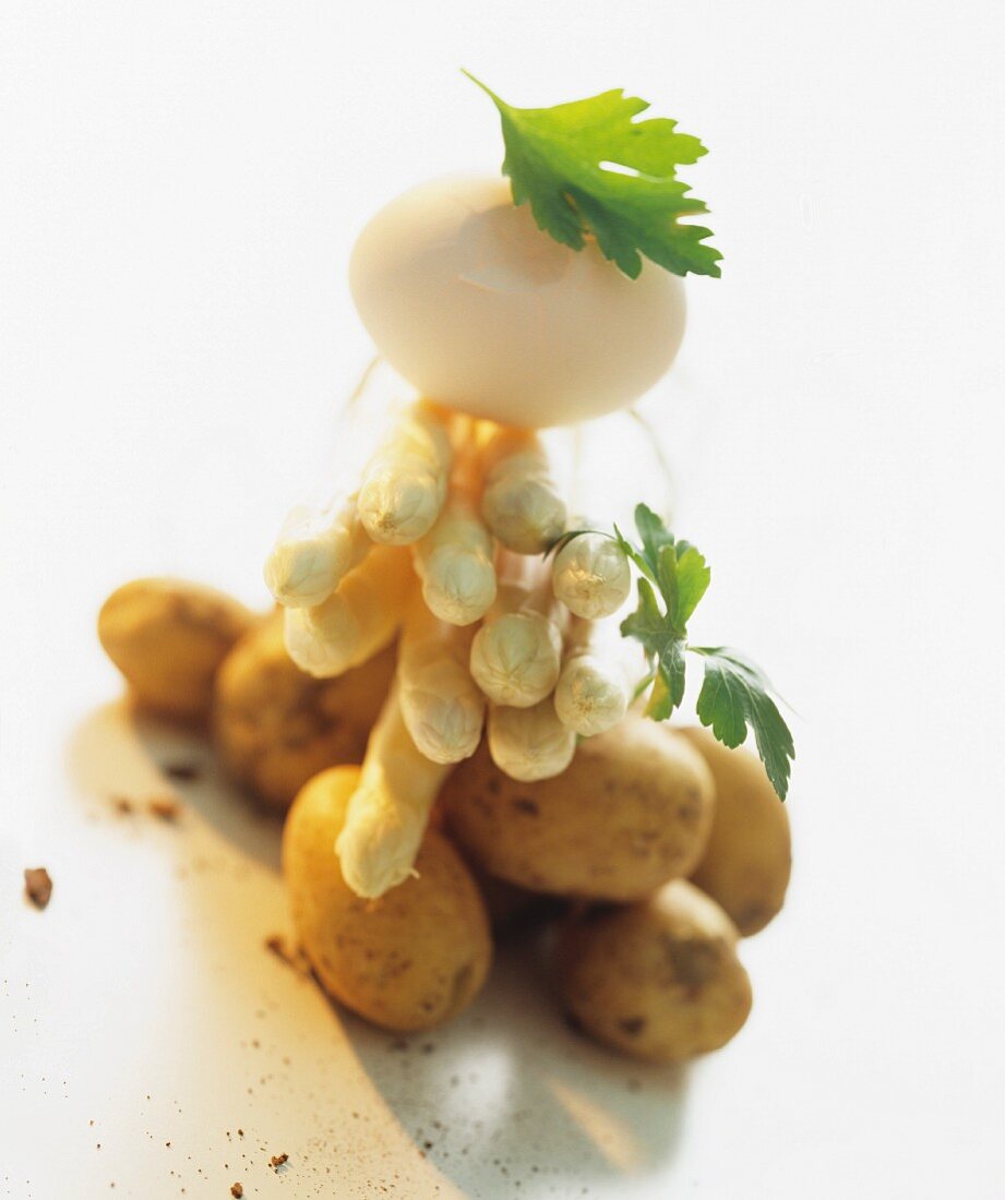 A still life of ingredients featuring white asparagus, potatoes and an egg