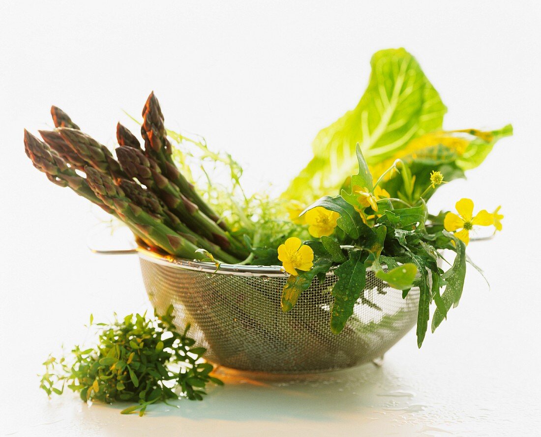 Green asparagus and assorted salad leaves in a colander