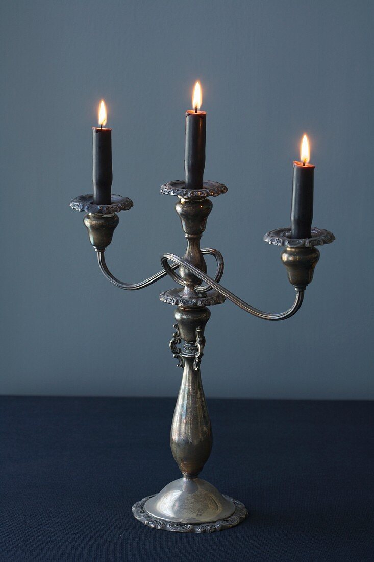 Dreiarmiger Kerzenleuchter mit schwarzen brennenden Kerzen
