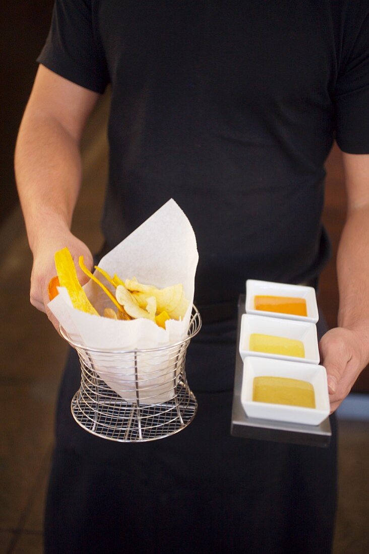 A Waiter Holding a Basket of Fried Plantain Chips with a Tray of Dipping Sauces